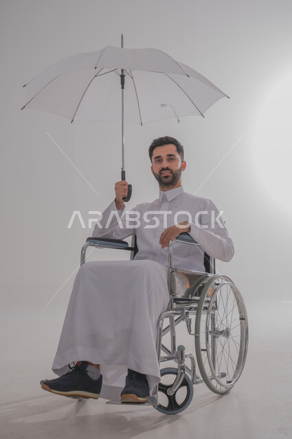الشتاء والاجواء الماطرة, ذوي الاحتياجات الخاصة والهمم، بورتريه  لرجل عربي خليجي سعودي يرتدي الثوب يجلس على كرسي متحرك ويحمل بيده شمسية، خلفية بيضاء