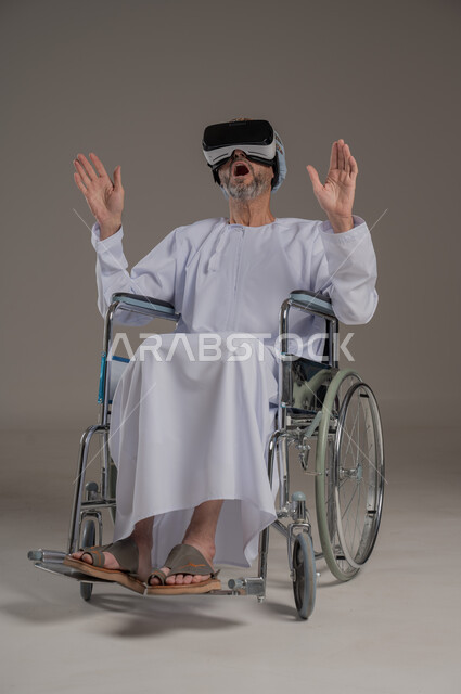  تحسين جودة حياة ذوي الاعاقة الحركية، استخدام كراسي المعاقين للمساعدة على الحركة والتنقل، بورتريه لرجل عربي  خليجي عماني يرتدي العمامة والدشداشة يقوم بمشاهدة أفلام عبر نظارات الواقع الافتراضي ثلاثية الأبعاد، محاكاة العالم الخيالي والتفاعل مع الفيلم، خلفية رمادية