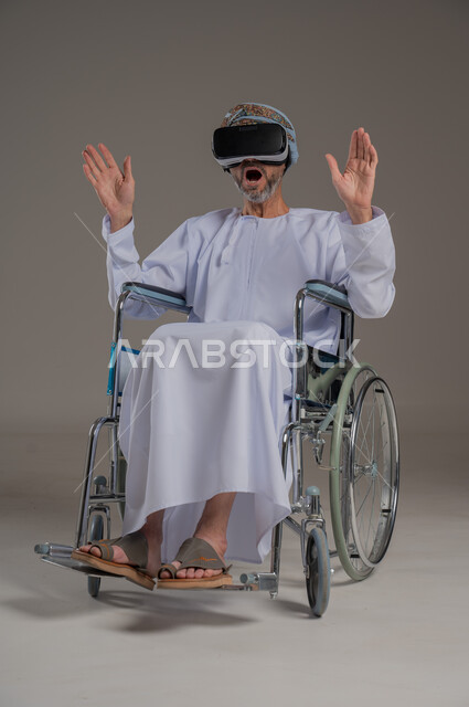  تحسين جودة حياة ذوي الاعاقة الحركية، استخدام كراسي المعاقين للمساعدة على الحركة والتنقل، بورتريه لرجل عربي  خليجي عماني يرتدي العمامة والدشداشة يقوم بمشاهدة أفلام عبر نظارات الواقع الافتراضي ثلاثية الأبعاد، محاكاة العالم الخيالي والتفاعل مع الفيلم، خلفية رمادية
