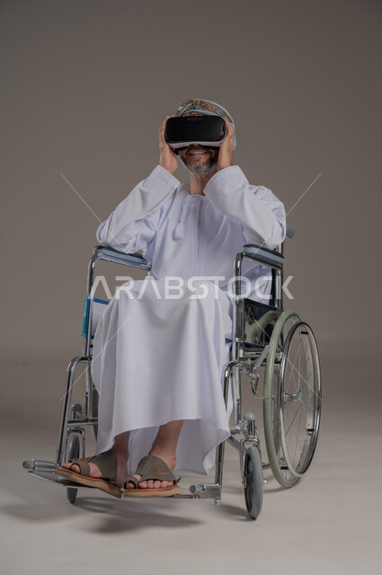 Simulating the imaginary world and interacting with the movie, improving the quality of life for people with motor disabilities, using wheelchairs to help with movement and mobility, portrait of an Arab Gulf Omani man wearing a turban and dishdasha watching movies through 3D virtual reality glasses, gray background