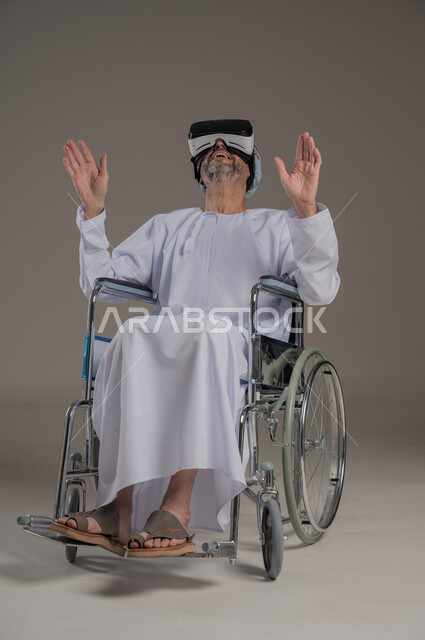محاكاة العالم الخيالي والتفاعل مع الفيلم، تحسين جودة حياة ذوي الاعاقة الحركية، استخدام كراسي المعاقين للمساعدة على الحركة والتنقل، بورتريه لرجل عربي  خليجي عماني يرتدي العمامة والدشداشة يقوم بمشاهدة أفلام عبر نظارات الواقع الافتراضي ثلاثية الأبعاد، خلفية رمادية