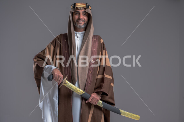 الوقوف باستقامة وشموخ، مفهوم الاصالة والعراقة عند العرب، بورتريه لرجل عربي خليجي سعودي يرتدي الدقلة والغترة والعقال الذهبي يحمل، يوم بدينا 22 فبراير, إحياء تراث المملكة, الاحتفالات بالمناسبات الوطنية, ذكرى تأسيس الدولة الأولى 1727م، خلفية رمادية