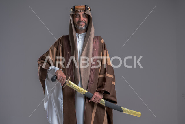 الوقوف باستقامة وشموخ، مفهوم الاصالة والعراقة عند العرب، بورتريه لرجل عربي خليجي سعودي يرتدي الدقلة والغترة والعقال الذهبي يحمل، يوم بدينا 22 فبراير, إحياء تراث المملكة, الاحتفالات بالمناسبات الوطنية, ذكرى تأسيس الدولة الأولى 1727م، خلفية رمادية