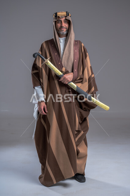 Celebrations of national occasions, pride and pride in national belonging, wearing traditional folk costumes, a portrait of a Saudi Gulf Arab man wearing a traditional costume and holding a sword in his hand, reviving the heritage of the Kingdom, the founding of the first Saudi state 1727 AD, the anniversary of Saudi Founding Day, gray background