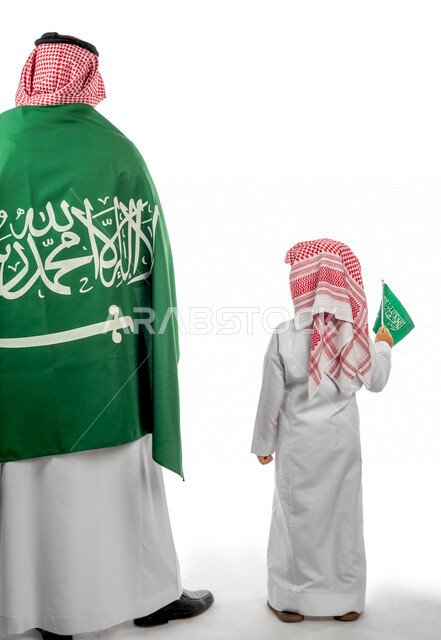 تصوير من الخلف لرجل عربي خليجي سعودي يضع على ظهره علم المملكة العربية السعودية ، طفل خليجي سعودي بيده علم المملكة ،  ذكرى اليوم الوطني السعودي ،الاحتفال بالعيد الوطني السعودي