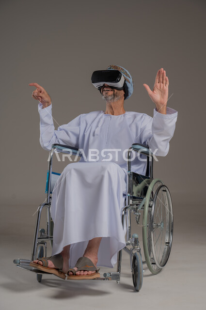 تحسين جودة حياة ذوي الاعاقة الحركية، محاكاة العالم الخيالي والتفاعل معه، استخدام كراسي المعاقين للمساعدة على الحركة والتنقل، بورتريه لرجل عربي  خليجي عماني يرتدي العمامة والدشداشة يقوم بمشاهدة أفلام عبر نظارات الواقع الافتراضي ثلاثية الأبعاد، خلفية رمادية