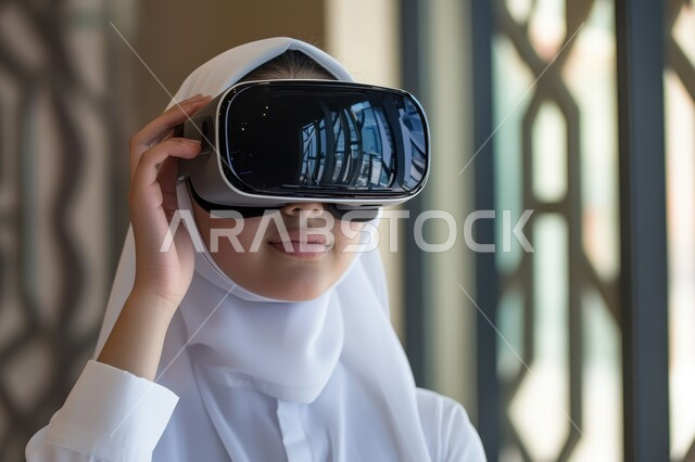 الاستمتاع في قضاء الأوقات الترفيهية عبر استخدام التقنيات الحديثة الالكترونية، شابة عربية خليجية سعودية محجبة تضع نظارات الفي آر ثلاثية الابعاد، الاندماج والتفاعل مع العالم الافتراضي، دمج التكنولوجيا بالحياة العملية