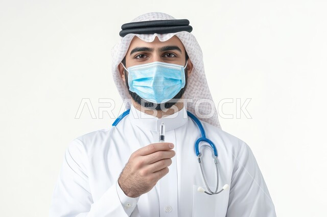 Ready to provide services to patients with all efficiency, concept of medicine and health care, close-up portrait of a smiling Saudi Arabian Gulf Arab doctor wearing traditional thobe and shemagh wearing a stethoscope and mask holding a medical syringe in his hand looking at the camera with an expression of self-confidence