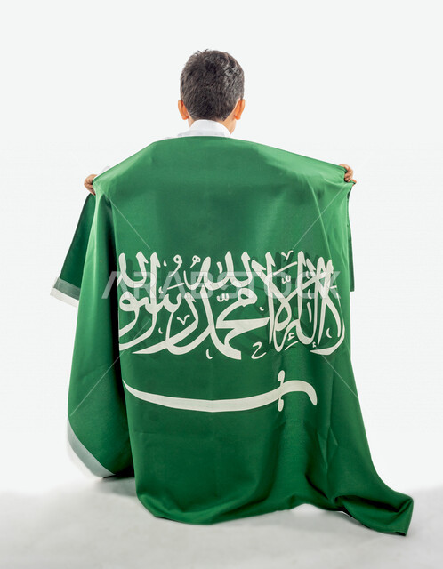 تصويرمن الخلف لطفل عربي خليجي سعودي يضع على ظهره علم المملكة العربية السعودية ، ذكرى اليوم الوطني السعودي ،الاحتفال بالعيد الوطني السعودي