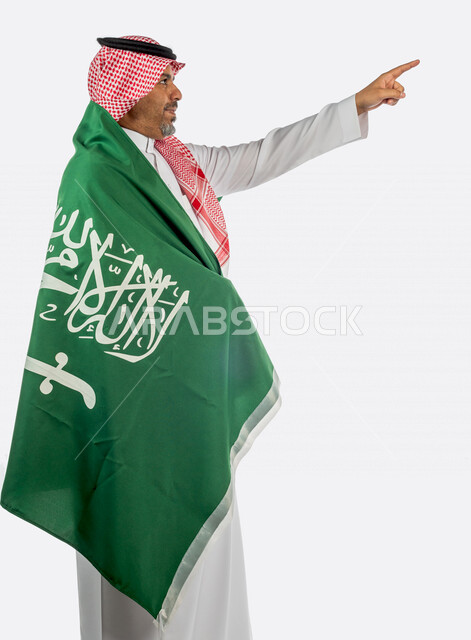 بورتريه رجل عربي خليجي سعودي يشير باصبع السبابة ، يضع على ظهره  علم المملكة العربية السعودية ، ذكرى اليوم الوطني السعودي ،الاحتفال بالعيد الوطني السعودي