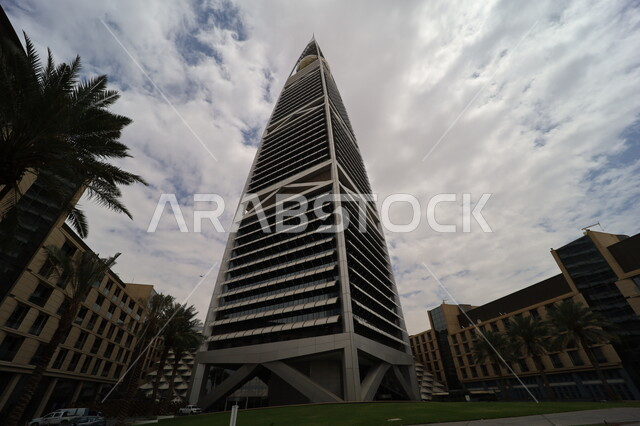 النمو والتطور العمراني في العاصمة، صورة من الاسفل لبرج الفيصلية في مدينة الرياض، الفن الهندسي المعماري للأبراج وناطحات السحاب في المملكة العربية السعودية، معالم ومباني مشهورة، منظر السماء المليئة بالغيوم البيضاء، الاهتمام بزراعة أشجار النخيل في المدن