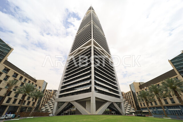 النمو والتطور العمراني في العاصمة، صورة من الاسفل لبرج الفيصلية في مدينة الرياض، الفن الهندسي المعماري للأبراج وناطحات السحاب في المملكة العربية السعودية، معالم ومباني مشهورة، منظر السماء المليئة بالغيوم البيضاء، الاهتمام بزراعة أشجار النخيل في المدن