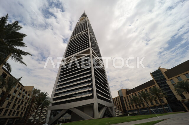 النمو والتطور العمراني في العاصمة، صورة من الاسفل لبرج الفيصلية في مدينة الرياض، الفن الهندسي المعماري للأبراج وناطحات السحاب في المملكة العربية السعودية، معالم ومباني مشهورة، منظر السماء المليئة بالغيوم البيضاء، الاهتمام بزراعة أشجار النخيل في المدن