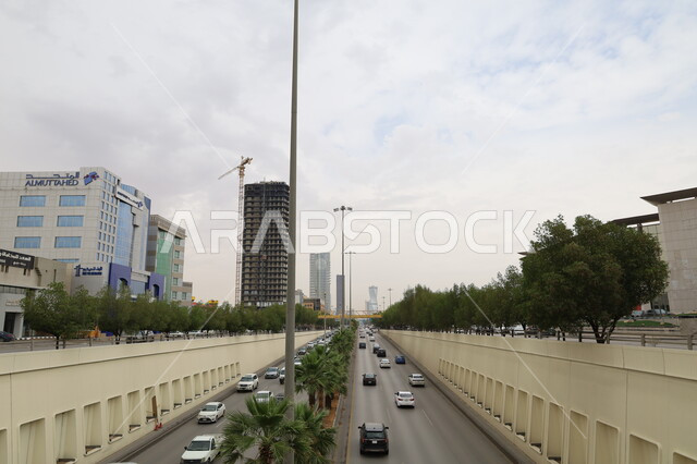 حركة مرور السيارات في المملكة العربية السعودية، منظر السماء المليئة بالغيوم البيضاء نهارا، الطرق والشوارع المعبدة،  نمط الحياة في البلد، التطور والتقدم العمراني، الفن الهندسي المعماري للأبراج في مدينة الرياض، الاهتمام بزراعة الأشجار والمروج والنباتات الخضراء