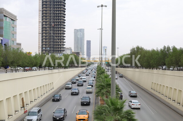 حركة مرور السيارات في المملكة العربية السعودية، منظر السماء المليئة بالغيوم البيضاء نهارا، الطرق والشوارع المعبدة،  نمط الحياة في البلد، التطور والتقدم العمراني، الفن الهندسي المعماري للأبراج في مدينة الرياض، الاهتمام بزراعة الأشجار والمروج والنباتات الخضراء