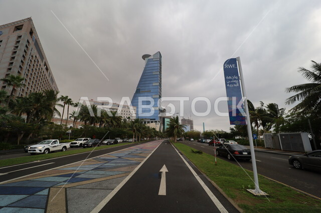 Famous tourist attractions in Saudi Arabia, the new Corniche Tower in the coastal city, the urban growth and development of facilities and skyscrapers in Jeddah, cloudy weather and overcast skies, palm trees and green plants on the roads of tourist cities, the colorful bicycle path in the streets