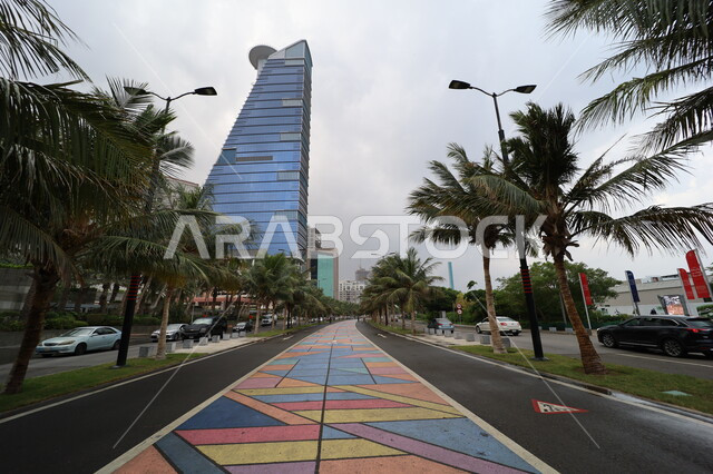 Famous tourist attractions in Saudi Arabia, the new Corniche Tower in the coastal city, the urban growth and development of facilities and skyscrapers in Jeddah, cloudy weather and overcast skies, palm trees and green plants on the roads of tourist cities, the colorful bicycle path in the streets