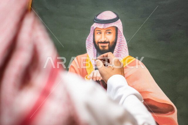 صورة مقربة من الخلف لفنان موهوب عربي خليجي سعودي يبدع برسم لوحة فنية خاصة بسمو ولي العهد محمد بن سلمان ، ذكرى اليوم الوطني السعودي ، الاحتفال بالعيد الوطني السعودي