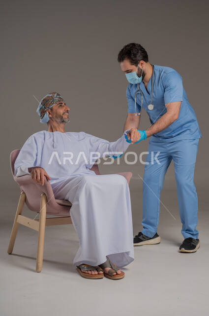 اجراءات الفحص الطبي العامة لكبار السن، بورتريه لممرض عربي خليجي  يلبس اليونيفورم والقفازات والكمامة الوقائية يقوم بفحص مريض عماني مسن يرتدي الدشداشة والعمامة يجلس على كرسي، استخدام الأدوات الطبية الحديثة، خلفية رمادية
