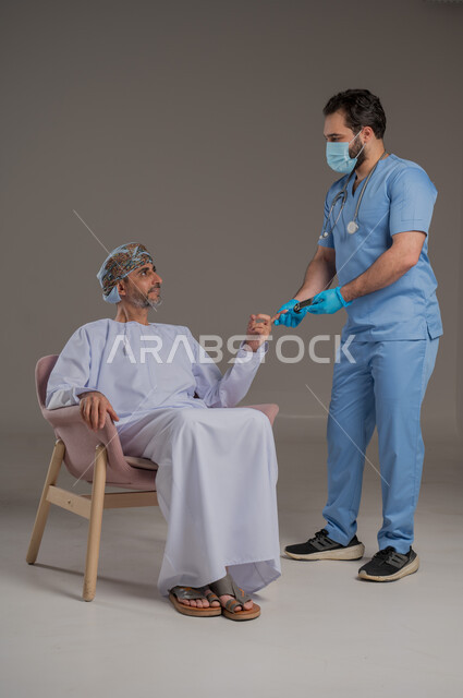 اجراءات الفحص الطبي العامة لكبار السن، بورتريه لممرض عربي خليجي  يلبس اليونيفورم والقفازات والكمامة الوقائية يقوم بفحص مريض عماني مسن يرتدي الدشداشة والعمامة يجلس على كرسي، استخدام الأدوات الطبية الحديثة، خلفية رمادية