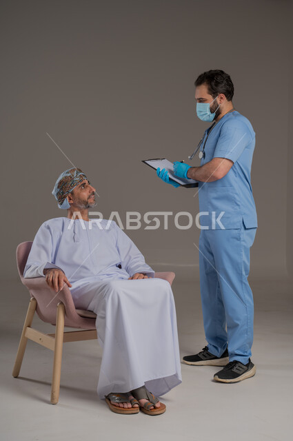 اجراءات الفحص الطبي العامة لكبار السن، بورتريه لممرض عربي خليجي  يلبس اليونيفورم والقفازات والكمامة الوقائية يقوم بفحص مريض عماني مسن يرتدي الدشداشة والعمامة يجلس على كرسي، استخدام الأدوات الطبية الحديثة، خلفية رمادية