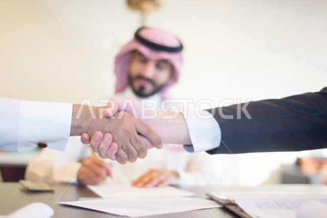 فريق عمل عربي خليجي سعودي، رجلان عربيان سعوديان يتصافحان بعد اجتماع عمل ناجح، زملاء عمل، شركاء عمل، شركة سعودية ناجحة، بيئة العمل