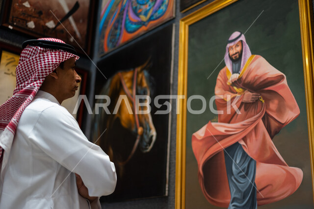 صورة لفنان عربي خليجي سعودي موهوب ينظر و يتأمل بلوحة فنية خاصة بسمو ولي العهد الأمير محمد بن سلمان ، ذكرى اليوم الوطني السعودي ، الاحتفال بالعيد الوطني السعودي