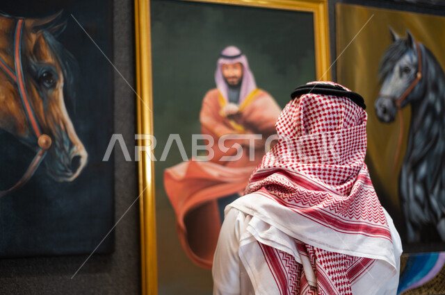 صورة من الخلف لفنان عربي خليجي سعودي موهوب ينظر و يتأمل بلوحة فنية خاصة بسمو ولي العهد الأمير محمد بن سلمان ، ذكرى اليوم الوطني السعودي ، الاحتفال بالعيد الوطني السعودي