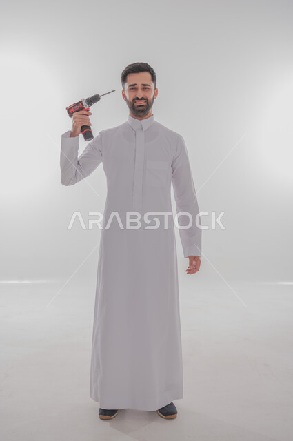 المهارة و اتقان العمل، استخدام أدوات ومعدات الصيانة لاجراء التصليحات، بورتريه لرجل عربي سعودي خليجي يرتدي الثوب التقليدي ينظر إلى الكاميرا بإيماءات البكاء يحمل بيده فرد ثاقب يوجهه نحو رأسه، الجسم بالطول الكامل، خلفية بيضاء 