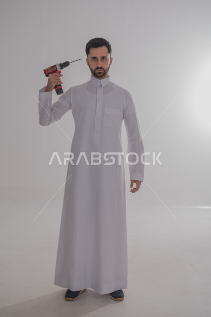 Skill and mastery of work, using maintenance tools and equipment to make repairs, portrait of a Saudi Arabian Gulf man wearing traditional thobe looking at the camera with angry gestures holding a piercing spear in his hand pointing it towards his head, full length body, white background