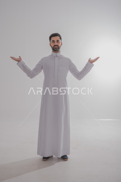 رفع اليدين في الهواء بتعابير الغضب، النظر للكاميرا بإيماءات الانزعاج وعدم الرضا، بورتريه لرجل عربي خليجي سعودي يرتدي الثوب التقليدي يرفع كفيه بتذمر وسخط، الجسم بالطول الكامل، خلفية بيضاء