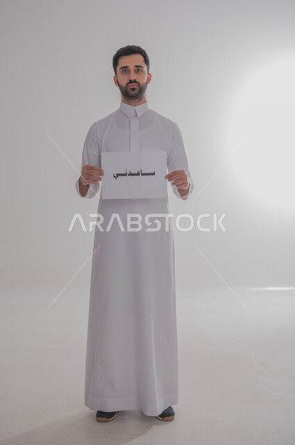 مفهوم طلب العون والمساعدة، لوحه بيضاء مربعه، استخدام لوحات توضيحية تعريفية، بورتريه لرجل عربي خليجي سعودي يرتدي الثوب التقليدي يحمل بيده موك اب مربع أبيض مكتوب عليه ساعدني، ينظر إلى الكاميرا، صورة الجسم بالكامل، خلفية بيضاء 