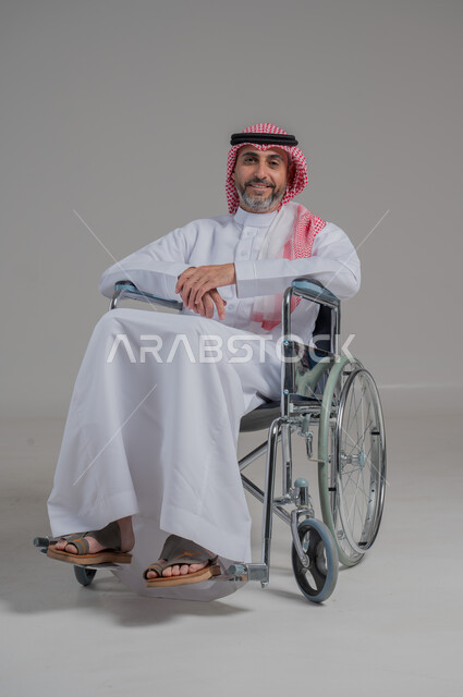 Poor motor ability and difficulty walking, portrait of a young Saudi Arabian Gulf man with special needs wearing traditional thobe and shemagh sitting in a wheelchair with cheerful and happy gestures on his face, full body, gray background