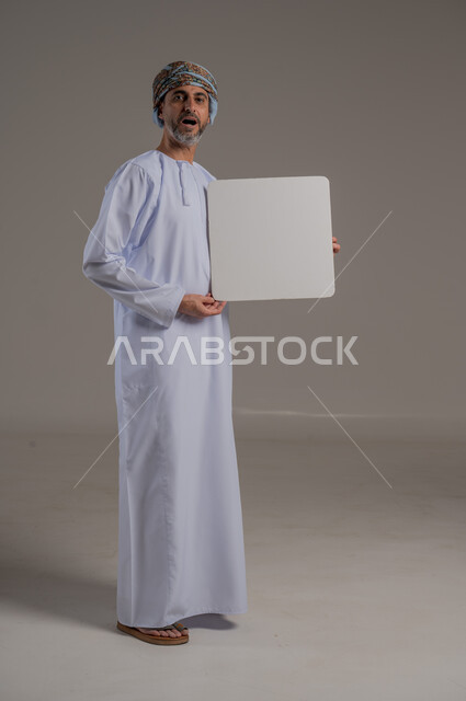 استخدام لوحات توضيحية تعريفية، إعلانات وعروضات تسويقية، لوحه بيضاء مربعه فارغة، بورتريه لرجل عربي خليجي عماني يرتدي دشداشة وعمامة يحمل بيده لافتة بيضاء وينظر بايماءات وجه مختلفة ، صورة الجسم بالطول الكامل، خلفية رمادي 