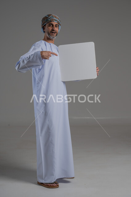 استخدام لوحات توضيحية تعريفية، إعلانات وعروضات تسويقية، لوحه بيضاء مربعه فارغة، بورتريه لرجل عربي خليجي عماني يرتدي دشداشة وعمامة يحمل بيده لافتة بيضاء وينظر بايماءات وجه مختلفة ، صورة الجسم بالطول الكامل، خلفية رمادي