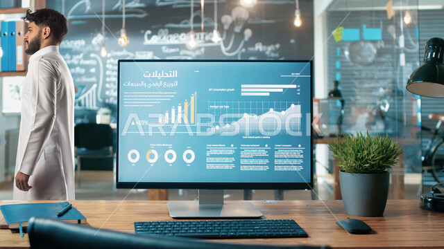 جهاز الكمبيوتر المحمول والكيبورد على مكتب في شركة سعودية بقسم التحليلات والإحصائيات البيانية،رجل سعودي خليجي، يقف في قسم التحليلات الرقمية، التحليلات والتوزيع الرقمي والمبيعات، وظائف ومهن، شاشة الكمبيوتر، الأسهم والرسوم البيانية والتوضيحية