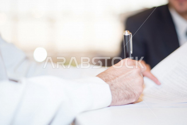 صورة مقربة لرجل اعمال عربي خليجي سعودي يمسك بيده قلم، توقيع عقد عمل بشركة سعودية خليجية، شركة سعودية، عقد عمل جديد، عقد شراكة، بيئة عمل