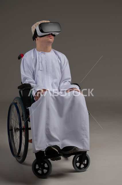 Simulating the imaginary world and interacting with the movie, improving the quality of life for people with motor disabilities, using wheelchairs to help with movement and mobility, portrait of an Arab Gulf Omani man wearing a kimmah and a dishdasha watching movies through 3D virtual reality glasses, gray background