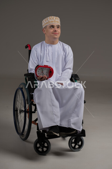 التذكيرات والتنبيهات الثابته، الدقة في المواعيد، بورتريه لرجل عربي خليجي عماني من ذوي الاحتياجات الخاصة يرتدي الدشاشة والكمة يجلس على كرسي متكرك يحمل بيده ساعة رقمية صغيرة, إنجاز المهامات في الوقت، ايماءات السعادة والسرور، خلفية رمادية