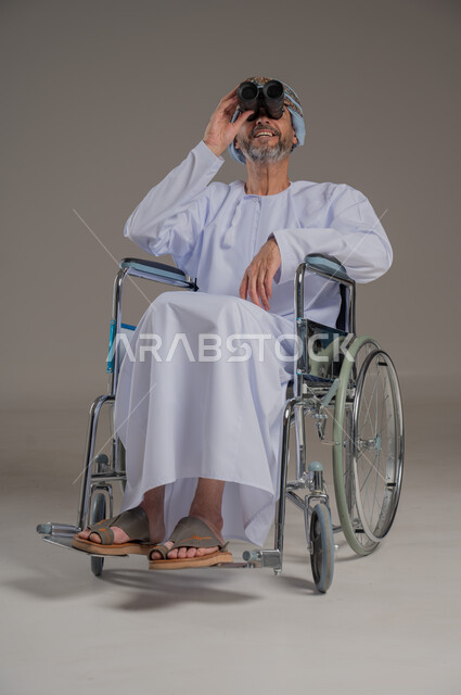 استعمال المنظار للكشف عن الاشياء البعيدة، ذوي الإحتياجات الخاصة والهمم, بورتريه لشاب عربي خليجي عماني من ذوي الاحتياجات الخاصة يرتدي العمامة والدشداشة يجلس على كرسي متحرك، خلفية رمادية
