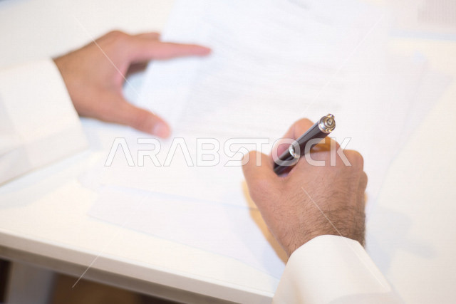 صورة مقربة لرجل اعمال عربي خليجي سعودي يمسك بيده قلم، توقيع عقد عمل بشركة سعودية خليجية، شركة سعودية، عقد عمل جديد، عقد شراكة، بيئة عمل