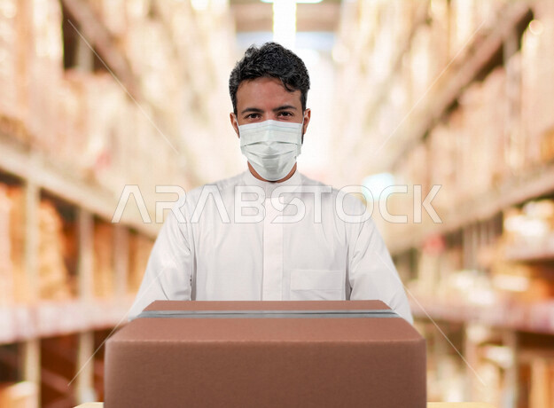 A young Saudi Arabian Gulf man, working in a warehouse warehouse, the concept of logistic business, shipping and transporting goods, taking into account the preventive measures against the Corona virus