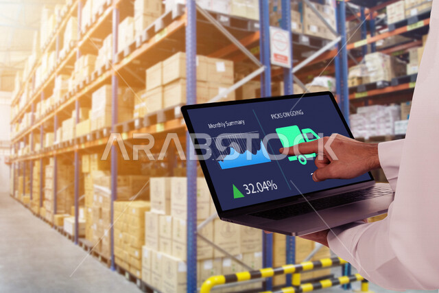 نظام ادارة المستودعات الذكي، صورة مقربة لمشرف اداري عربي سعودي خليجي ينظم ادارة المخازن عن طريق جهاز الابتوب المحمول، الإشراف على المستودعات و المخازن من خلال انظمة ذكية، الإشراف على عمليات الاستلام والتخزين والتوزيع والصيانة باستخدام تقنيات متطورة