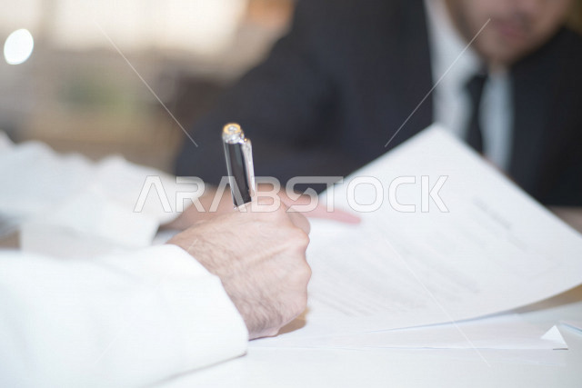صورة مقربة لرجل اعمال عربي خليجي سعودي يمسك بيده قلم، توقيع عقد عمل بشركة سعودية خليجية، شركة سعودية، عقد عمل جديد، عقد شراكة، بيئة عمل