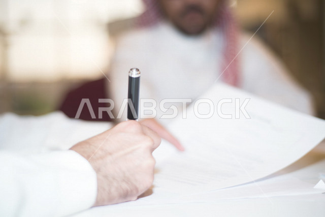 صورة مقربة لرجل اعمال عربي خليجي سعودي يمسك بيده قلم، توقيع عقد عمل بشركة سعودية خليجية، شركة سعودية، عقد عمل جديد، عقد شراكة، بيئة عمل