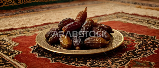 طبق نحاسي مليء بحبات التمر الصحي على السجادة، ضيافة تقليدية في الأعياد والمناسبات الدينية، أنواع التمور الفاخرة في المملكة العربية السعودية, ثمار ومحاصيل زراعية محلية وطنية، وجبة ذات قيمة غذائية عالية