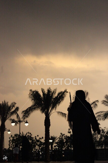 Palm trees and landscapes, nature view, clouds and fog during sunset, silhouette of a Saudi Gulf Arab woman walking in the streets of the Kingdom of Saudi Arabia