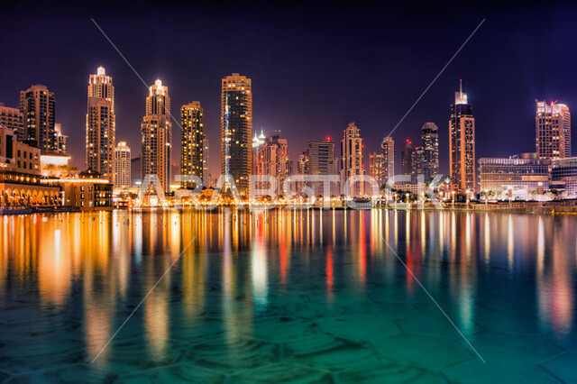 Urban growth and progress, urban development and the establishment of coastal tourist cities in Dubai, the advanced architectural art of commercial and residential facilities, luxury buildings and resorts in the United Arab Emirates, the reflection of the image of skyscrapers and illuminated towers at night on the sea waters