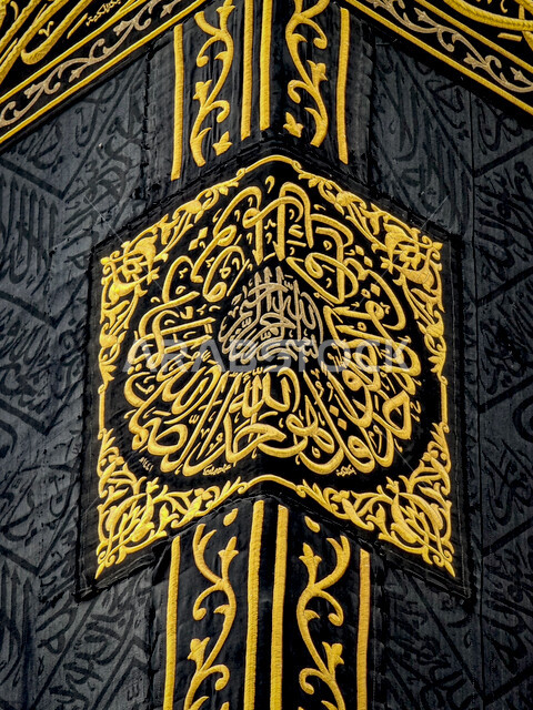 صورة مقربة لكسوة الكعبة المشرفة مغطاة بقماش من  الحرير الأسود مزينة بنقوش و زخارف من خيوط دهبية اسلامية و نصوص قرآنية ،المسجد الحرام في مكة المكرمة ، المملكة العربية السعودية 