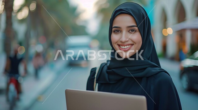 ملابس محجبات عصرية راقية، مفهوم الانوثة والنعومة،  الاهتمام بالمظهر الخارجي والأناقة، صورة مقربة لامرأة عربية خليجية سعودية محجبة تنظر إلى الكاميرا بايماءات الثقة بالنفس والسرور وتحمل بيدها جهاز تابليت